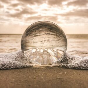 A crystal ball resting on Bonita Springs beach reflecting ocean waves at sunset.